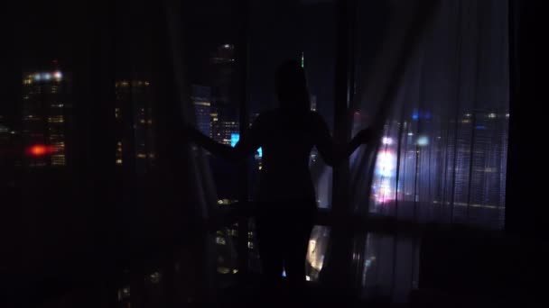 难以辨认的女人在夜里拉开窗帘，露出下面的时代广场. — 图库视频影像