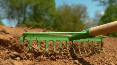 Tanınmayan çiftçi, büyük bir toprak yığınını metal tırmıkla dümdüz ediyor..
