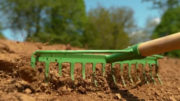 Tanınmayan çiftçi, büyük bir toprak yığınını metal tırmıkla dümdüz ediyor.. — Stok video