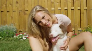 Gülümseyen kadın kameraya bakarken sevimli tüylü beyaz köpeğini okşar.