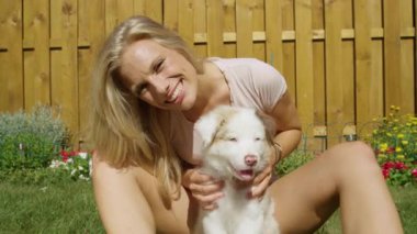 Mutlu sarışın kız güneşli bir günde köpeğini arka bahçede okşuyor..