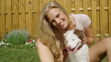 Genç bir kadın güneşli bir günde sevimli köpeğiyle kucaklaşırken eğleniyor..