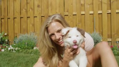 Beyaz tüylü bir köpek yavrusunu tutarken neşeli, beyaz bir kız gülümsüyor..