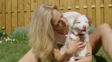 Gülümseyen kız bahçede oynarken pofuduk beyaz köpeği öpüyor.