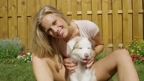 SLOW MOTION: Gelukkig blond meisje aaien haar hond in de achtertuin op een zonnige dag. — Stockvideo