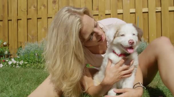CLOSE UP: Smiling girl kisses the fluffy white puppy while playing in the yard — Stock Video