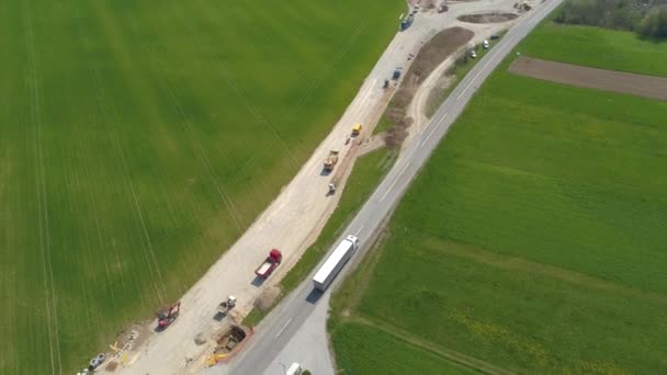 AERIAL: Vrachtwagen en auto rijden langs de lege weg die langs de bouwplaats leidt. — Stockvideo