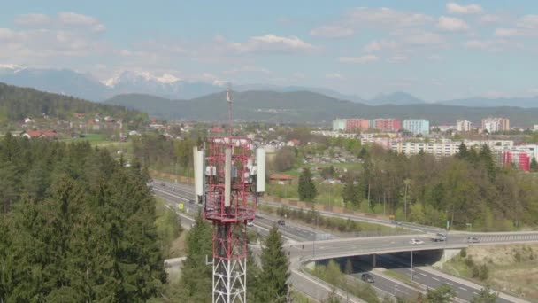 AERIAL: Flyger runt ett rött och vitt telekommunikationstorn vid motorvägen. — Stockvideo