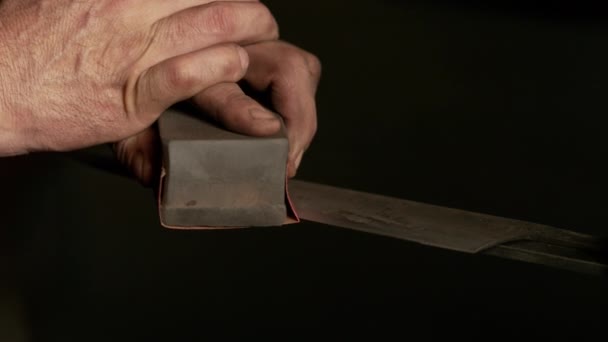 CLOSE UP: Unrecognizable bladesmith manually sharpens a newly forged knife. — Stock Video