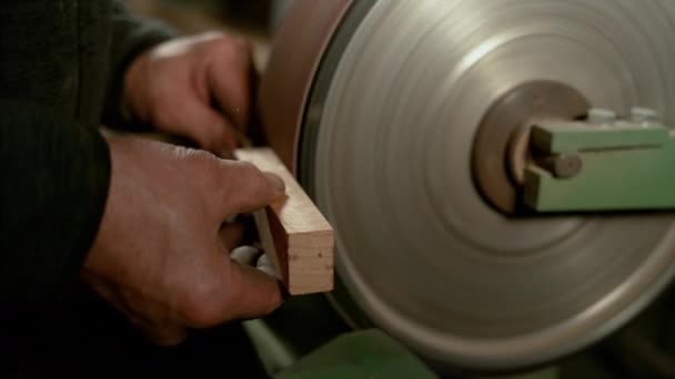 CLOSE UP: Столяр держит кусок дерева у колеса, покрытого наждачной бумагой — стоковое видео