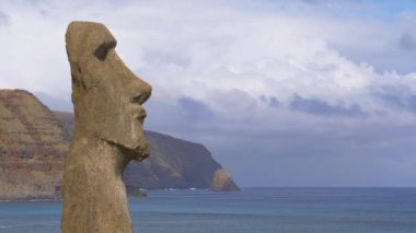 İnsan özelliklerine sahip büyük volkanik heykel derin mavi okyanusa bakıyor..