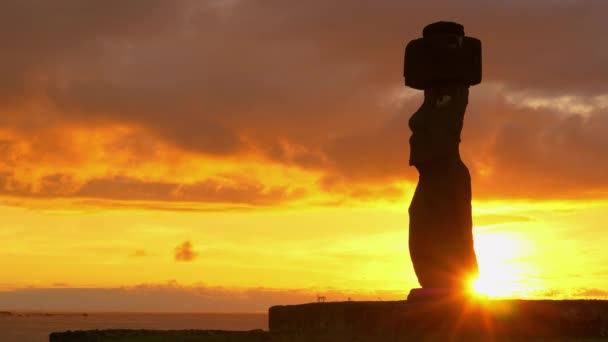 LÅNGA: Sommarsolnedgången lyser upp havet bakom det fascinerande moai. — Stockvideo