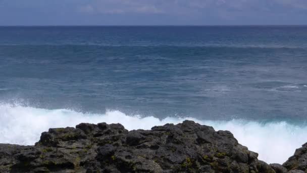 FERMER : De grosses vagues s'écrasent sur les roches volcaniques noires de la rive éloignée . — Video