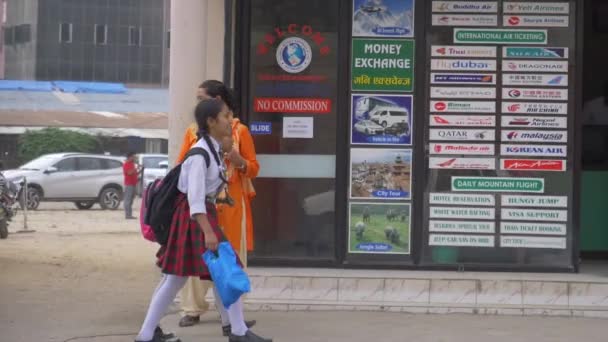 İki liseli kız, Katmandu 'da yol kenarındaki bir takas ofisinin önünden geçiyor.. — Stok video