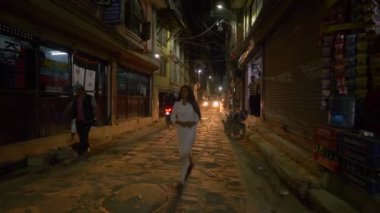 Arabalar ve motorsikletler karanlık caddede yürüyen insanların yanından geçiyor..