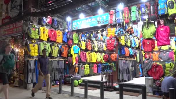 Turistas e moradores passam por uma loja que vende equipamentos de caminhada e jaquetas à noite . — Vídeo de Stock