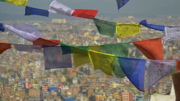 Sluiten omhoog: Veelkleurige gebedsvlaggen fladderen over de stad Kathmandu in de rug. — Stockvideo