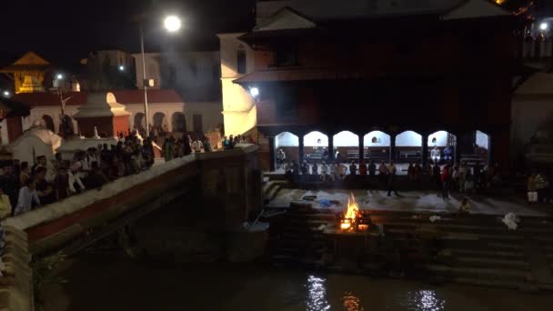 Menschen betrachten eine Luftbegräbniszeremonie von einer Brücke über den Bagmati-Fluss. — Stockvideo