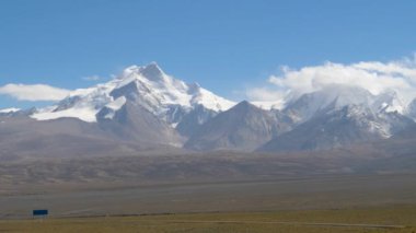 Uçsuz bucaksız kayalık düzlükler güneşli Tibet 'teki görkemli karlı dağlara doğru yol alır.