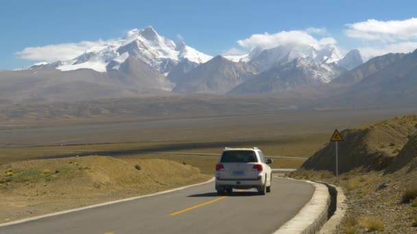 SUV branco desce uma estrada de asfalto vazia que leva às montanhas nevadas. — Vídeo de Stock