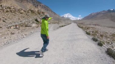 Enerjik adam Everest Dağı 'nın zirvesini işaret ediyor ve çakıl yolundan aşağı koşuyor..