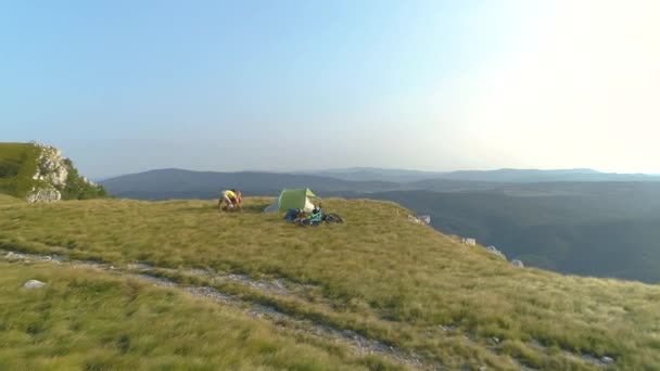 AERIAL: Überfliegendes Mountainbike-Paar bereitet Zelt in den Bergen vor. — Stockvideo