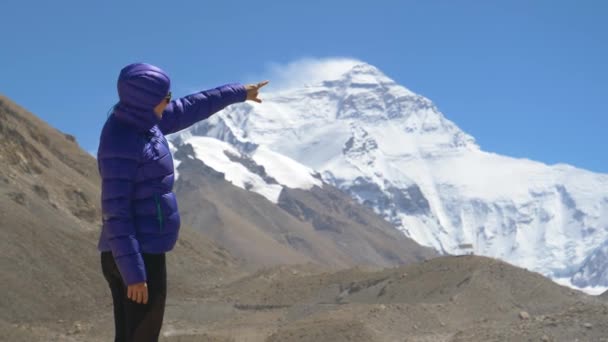 Бодрая белая женщина указывает на ветреную вершину Эвереста. — стоковое видео