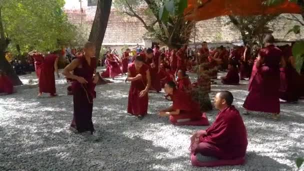 Mniši v tmavočerveném rouchu stojí a sedí a debatují před turisty. — Stock video