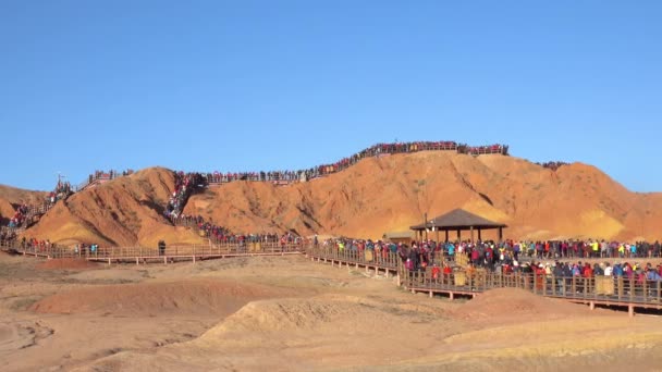 Masas de turistas se mueven a lo largo de las pasarelas que suben una colina en las montañas de Danxia — Vídeos de Stock