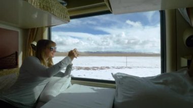 Kadın, tren yolculuğu sırasında karlı Tibet manzarasının fotoğraflarını çekiyor..
