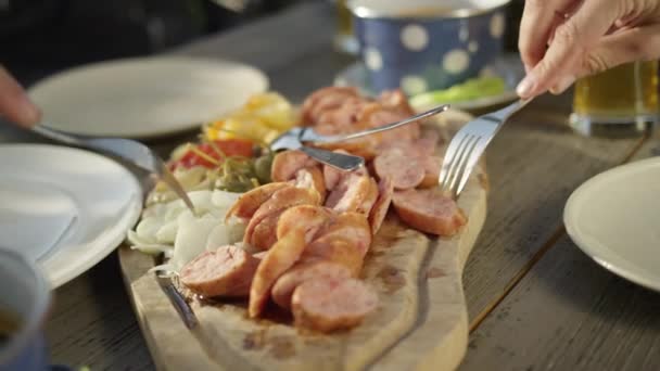 FERMETURE : Des amis s'assoient à la table de pique-nique et mangent des saucisses sur la planche à découper — Video
