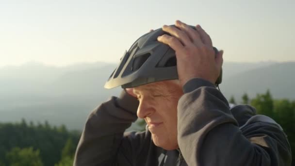 CLOSE UP: Older man puts on a helmet before a bicycle ride on a sunny evening. — Stock Video