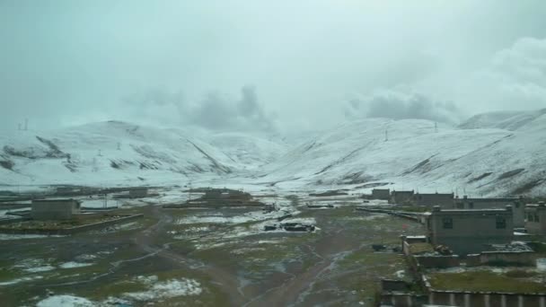 Espectacular vista de suaves colinas cubiertas de nieve detrás de una pequeña ciudad rural en el Tíbet — Vídeos de Stock