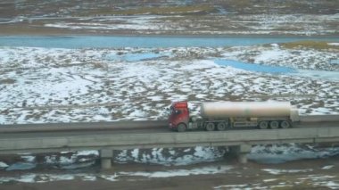 Eski kırmızı yük kamyonu, küçük akıntılarla dolu geniş bir ovayı geçiyor..