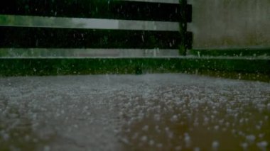Yağmur damlaları ve yumuşak dolu verandaya düşer ve durgun suyu damlatır.