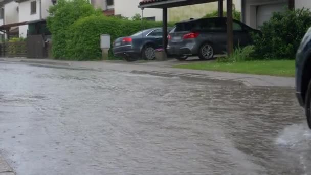 Κοντινό πλάνο: Μπλε SUV οδηγεί μέσα από τους πλημμυρισμένους δρόμους μιας προαστιακής γειτονιάς — Αρχείο Βίντεο