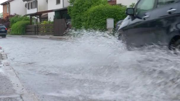 CLOSE UP: Två bilar kör ner översvämmade gatan förbi rowhouses under en regnstorm. — Stockvideo