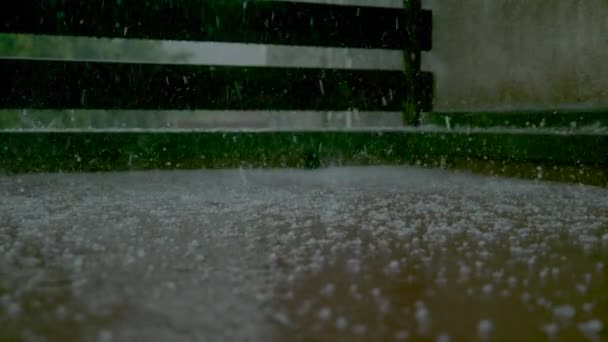 CLOSE UP: Regendruppels en zachte hagel vallen op de natte veranda en spatten stilstaand water — Stockvideo