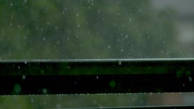 Yağmur damlalarının ıslak balkon korkuluklarına düşüşünün sinematik görüntüsü.