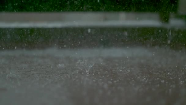 MACRO, DOF: Las gotas de lluvia caen en un pequeño charco que se forma en el suelo de un balcón — Vídeo de stock