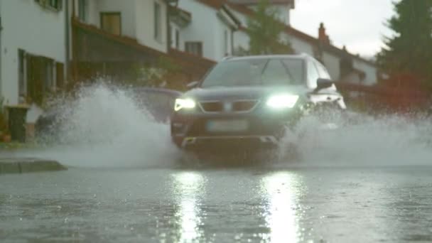 LOW Kąt: Niebieski SUV z oślepiającymi reflektorami przejeżdża wzdłuż zalanej ulicy. — Wideo stockowe