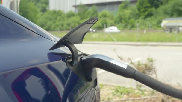 Κοντινό πλάνο, DOF: υψηλής τεχνολογίας ηλεκτρικό αυτοκίνητο Tesla φορτίζει σε ένα σταθμό στην άκρη του δρόμου. — Αρχείο Βίντεο