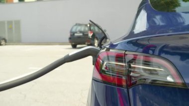 Parlak, yeni bir Tesla arabasının bir otoparkta şarj olurken detaylı görüntüsü..