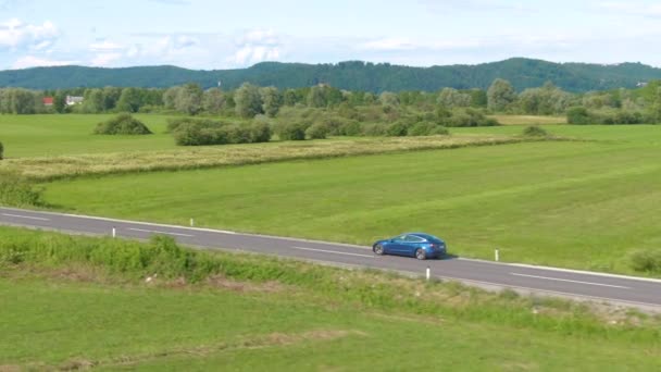 DRONE: Volando a lo largo de un coche autónomo que conduce por la carretera de campo recta. — Vídeo de stock