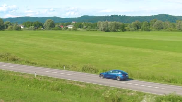 AERIAL: Кінематографічна зйомка нової Tesla Model 3, що їде по сільській дорозі. — стокове відео