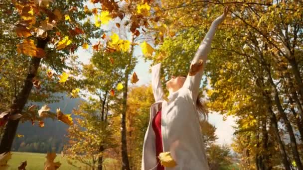 CLOSE UP Femme jette un tas de feuilles colorées dans l'air tout en marchant dans le parc 