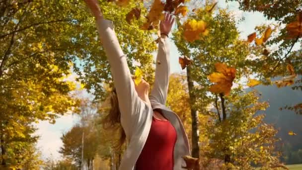 CERRAR: Chica despreocupada lanzando hojas secas al aire durante un paseo por el parque — Vídeo de stock