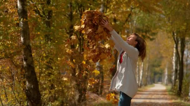 COPY SPACE: Vreugdevolle vrouw gooit een stapel herfst gekleurde bladeren hoog in de lucht. — Stockvideo