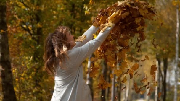 CLOSE UP: Жінка простягає руки після того, як кидає купу листя в повітрі . — стокове відео