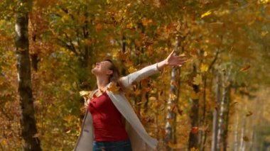 Kuru yapraklar gölgeliklerden düşerken kız kolları açık bir şekilde dönüyor.